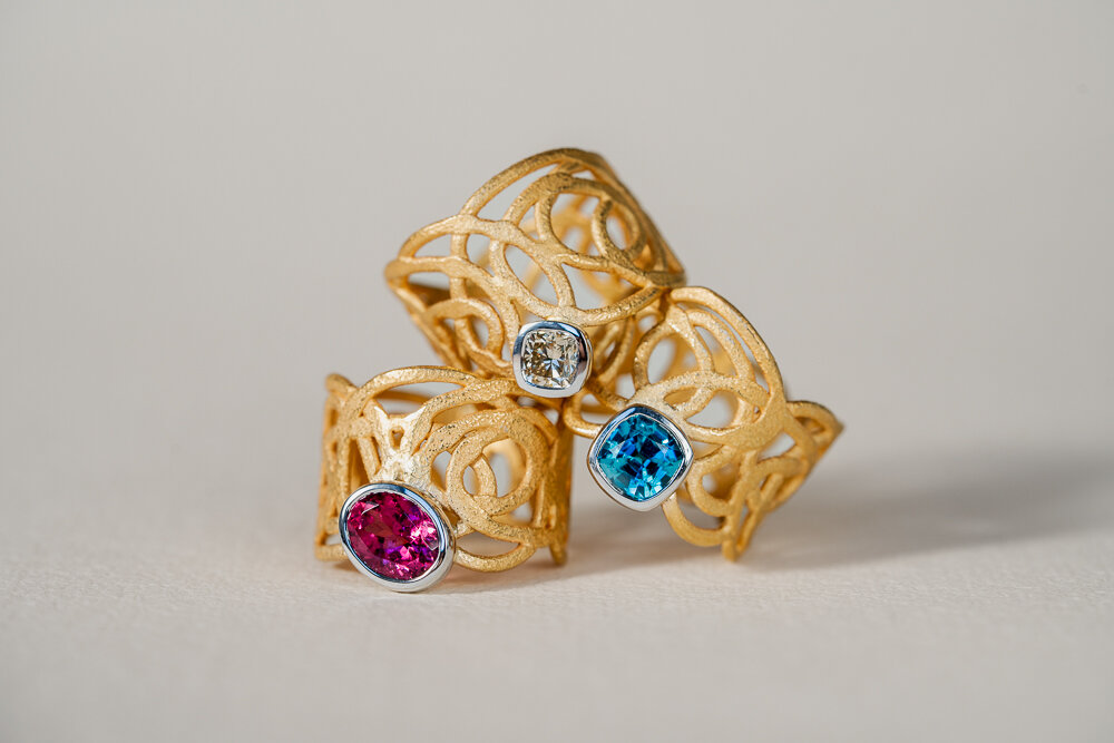 Drei goldene Ringe mit einem weißen, einem blauen und einem lila Diamanten