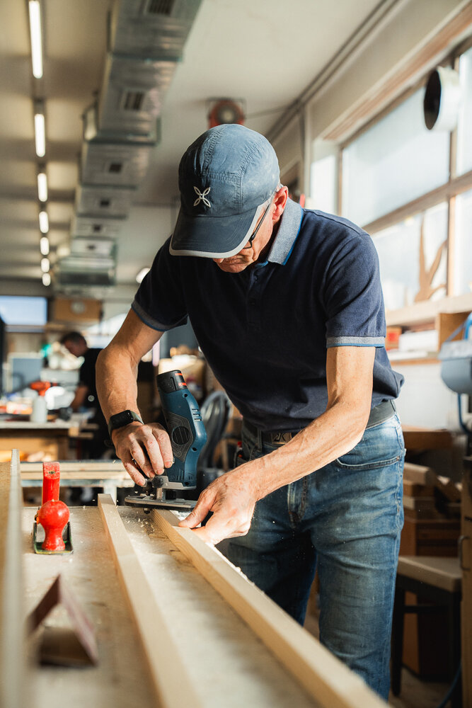 Ein Mann in einer Werkstatt, der ein Stück Holz mit einem Hobel bearbeitet.