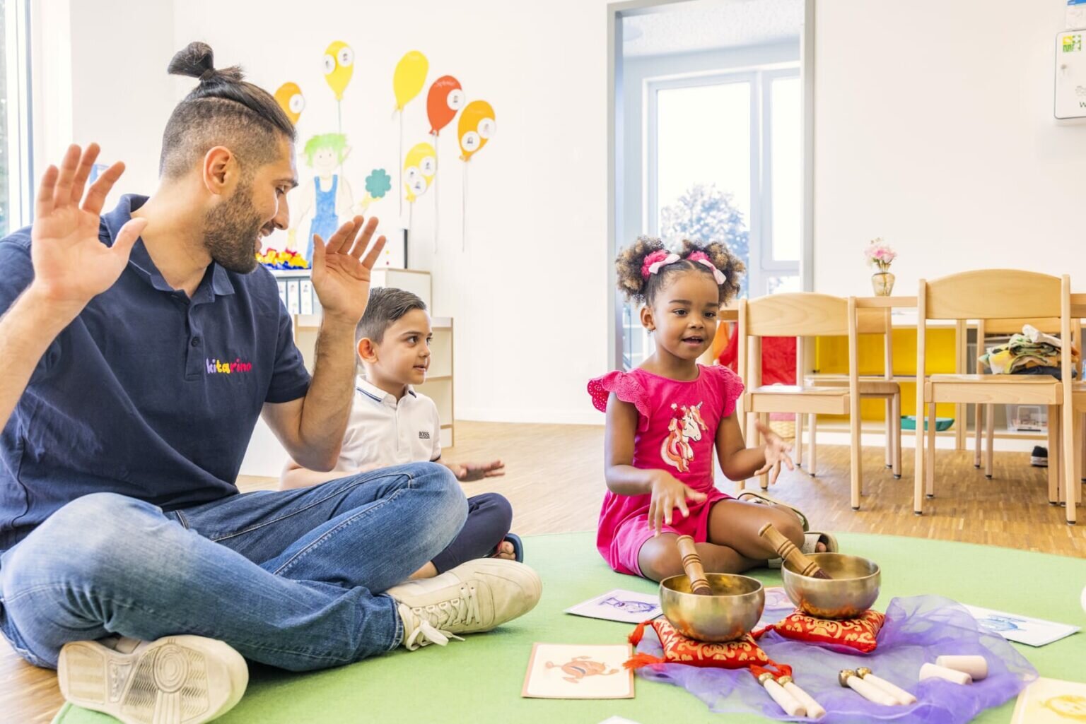 Ein Kindergärtner wie er mit zwei Kindern spielt